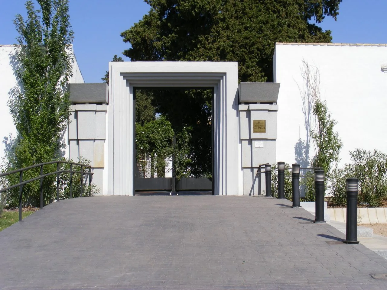 Puerta de la Fuensanta del cementerio de San Rafael de Córdoba, de líneas modernas entre muros blancos, con una rampa de acceso