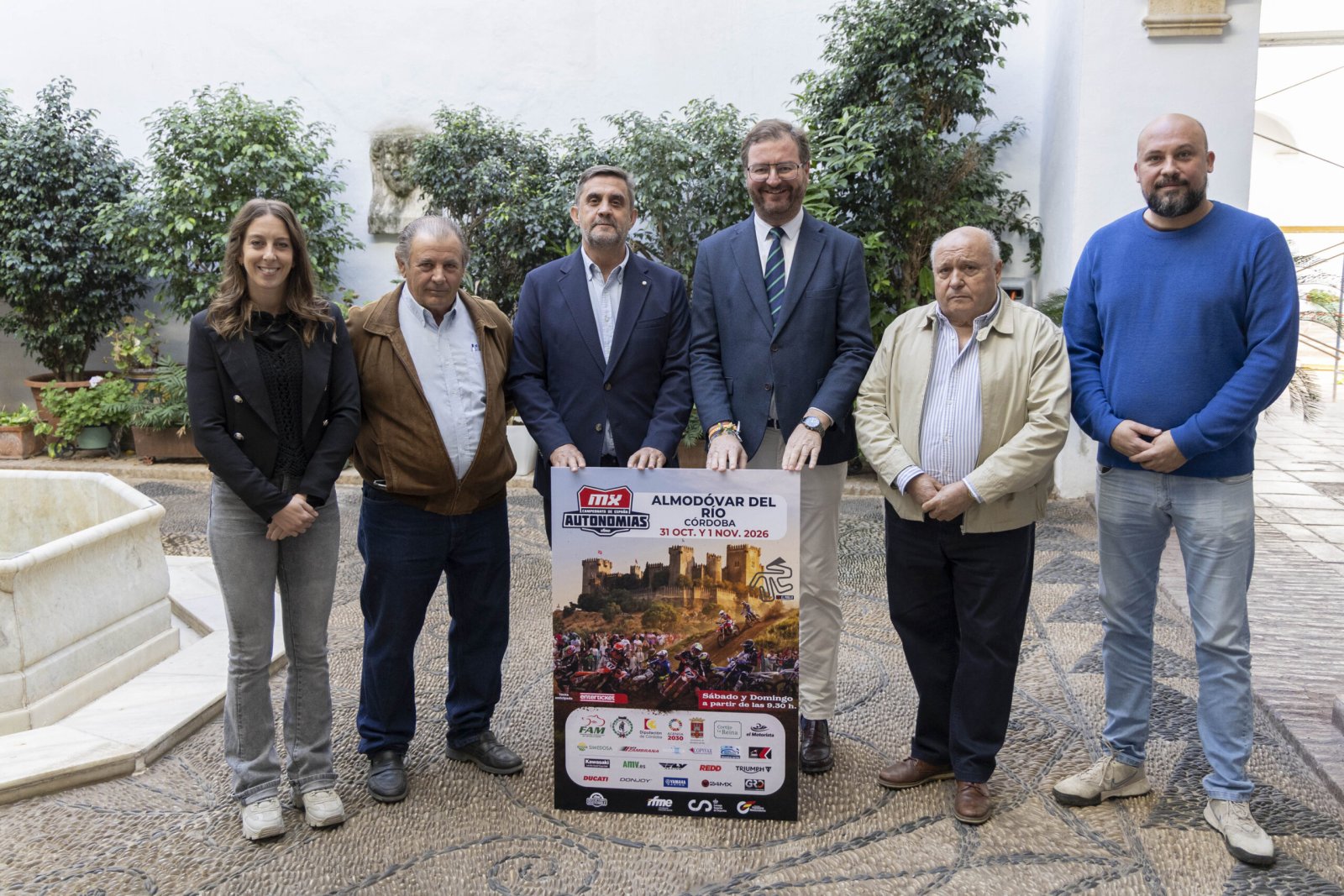 Seis personas posan en un patio junto a un cartel del Campeonato de España de Motocross en Almodóvar del Río.