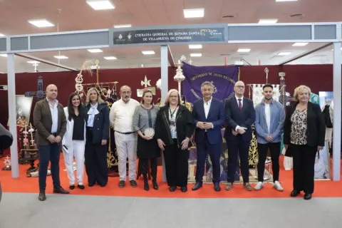Diez personas posan en fila sobre una alfombra roja ante el expositor de una cofradía de Semana Santa, con estandartes y objetos religiosos al fondo.