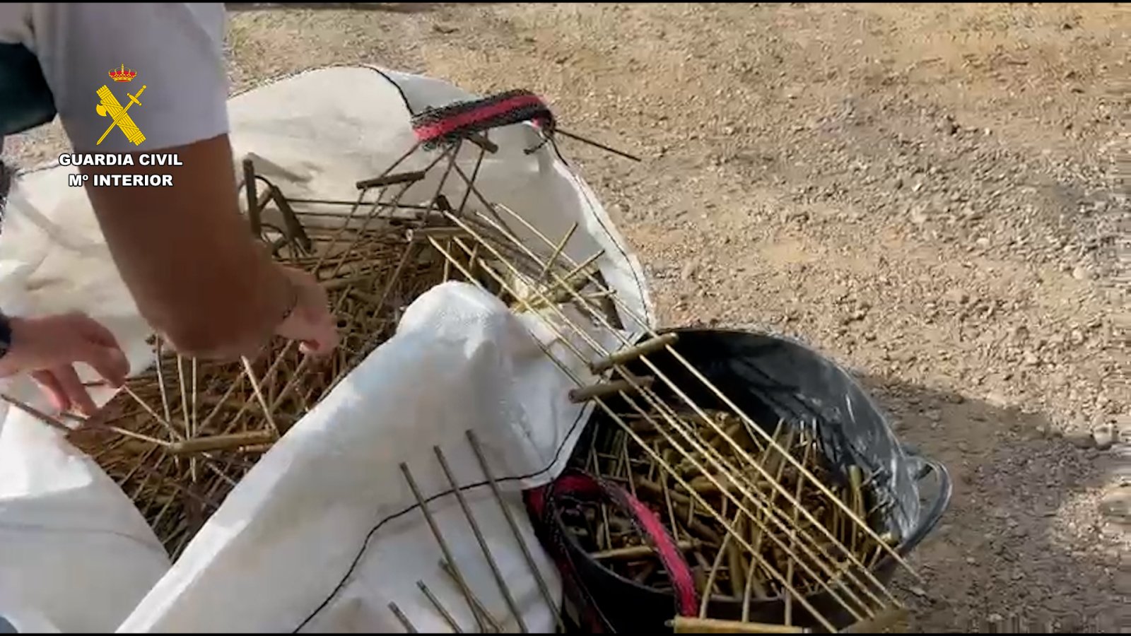Unas manos sostienen varias barandillas metálicas oxidadas sobre sacos blancos y una bolsa negra, en el suelo.