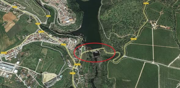 Vista aérea de un embalse entre un núcleo urbano y campos de cultivo, con una presa rodeada por un óvalo rojo.