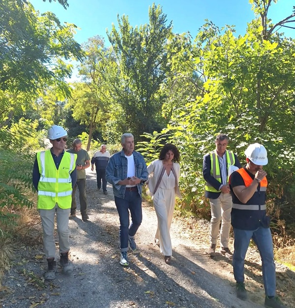 Un grupo de personas camina por un sendero de tierra entre vegetación, algunas con chalecos reflectantes y cascos.