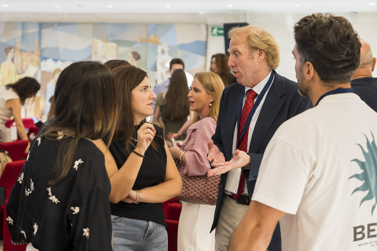 Un grupo de personas conversa de pie en una sala con butacas rojas y un mural al fondo.
