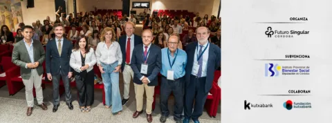 Siete personas de pie, sonriendo en una sala con butacas rojas y público sentado al fondo.