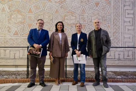 Cuatro personas de pie ante un gran mosaico geométrico romano, dos de ellas con folletos en la mano.