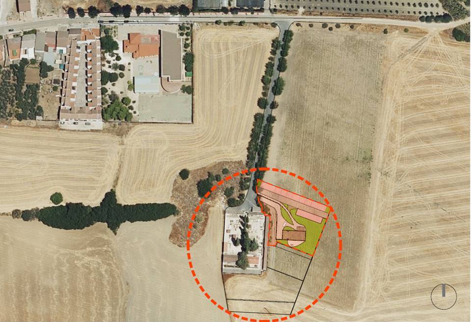 Vista aérea de campos de labor junto a una carretera y un edificio, con una zona delimitada por un círculo rojo discontinuo.
