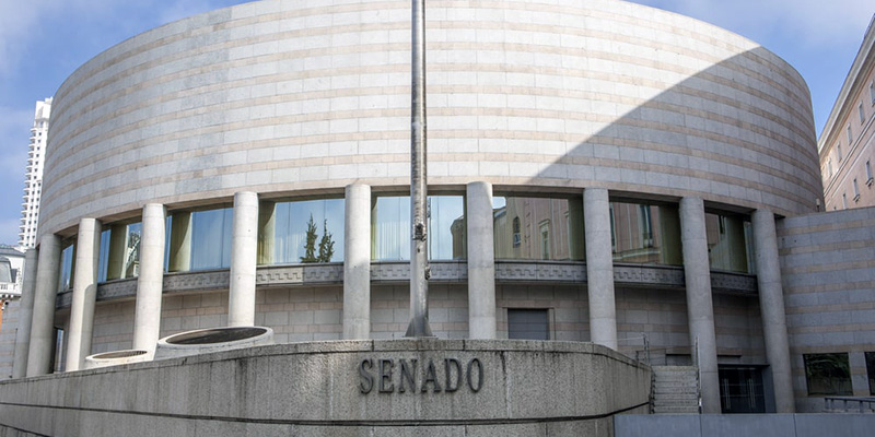 Edificio curvo de piedra clara con ventanales y columnas, y la palabra SENADO en el muro inferior.