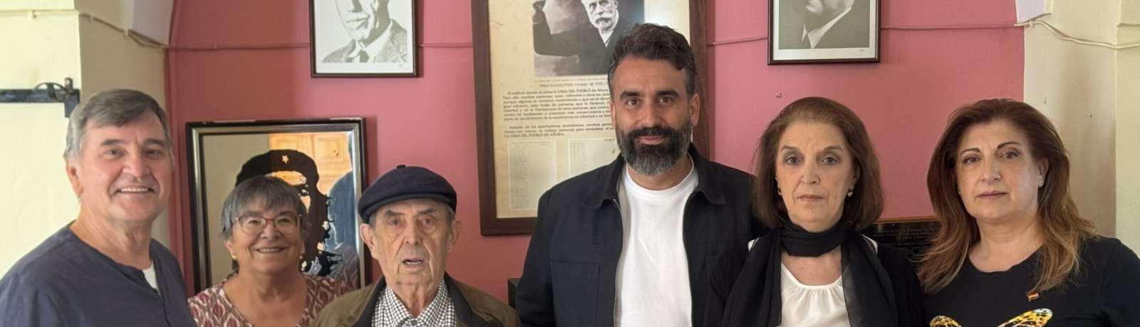 Cinco personas posan en una sala con paredes rosas y retratos enmarcados al fondo.