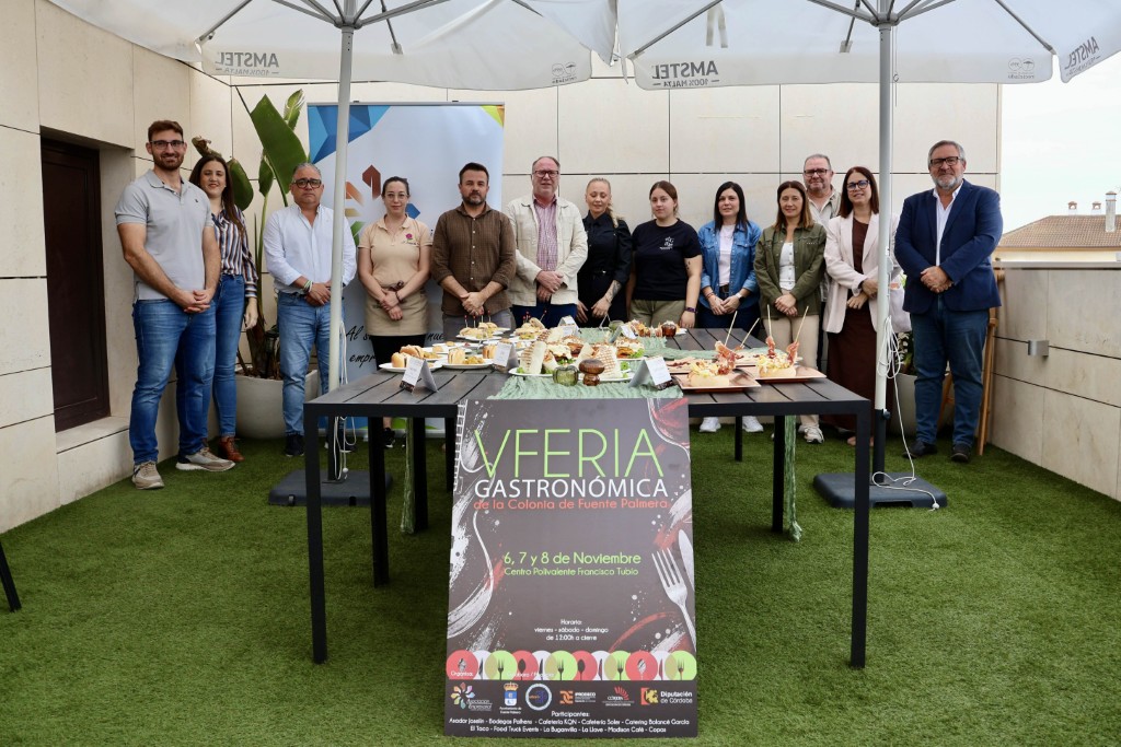 Un grupo de doce personas posa tras una mesa con tapas y un cartel de Feria Gastronómica sobre césped artificial.