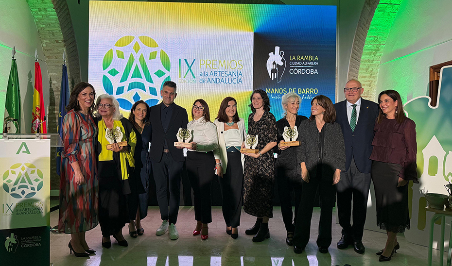 Un grupo de personas posa en fila sobre un escenario, varias con trofeos, ante una pantalla con el texto de unos premios de artesanía.