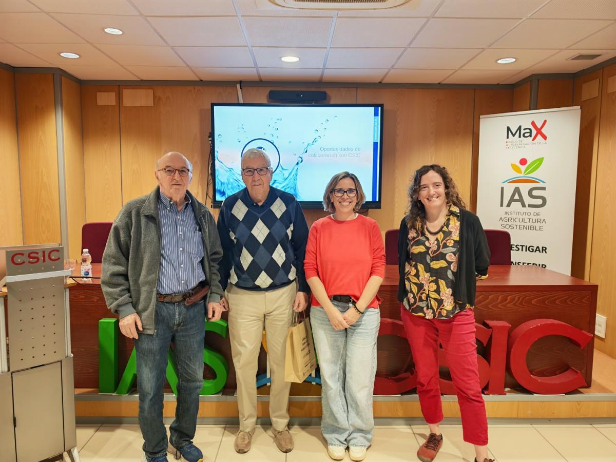 Cuatro personas de pie sonriendo ante una pantalla y un cartel del IAS-CSIC en una sala.