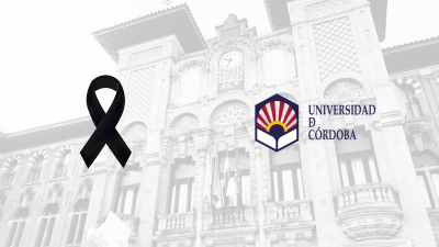 Lazo negro y logotipo de la Universidad de Córdoba sobre una fachada clara con reloj y balcones.