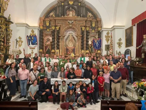 Un grupo numeroso de personas posa en el interior de una iglesia ante un retablo barroco, con sacerdotes entre ellos.