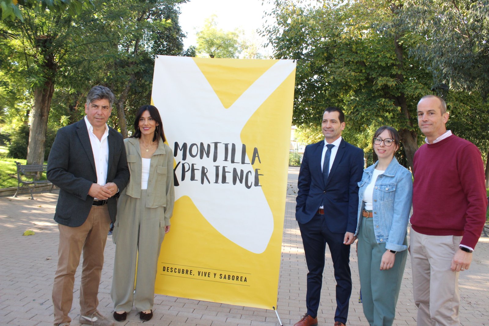 Cinco personas de pie junto a un cartel amarillo y blanco con el texto Montilla Xperience en un parque.