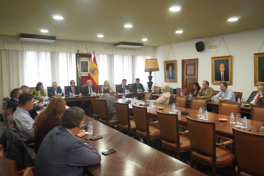 Varias personas sentadas alrededor de una gran mesa de reuniones en una sala con banderas y retratos en las paredes.